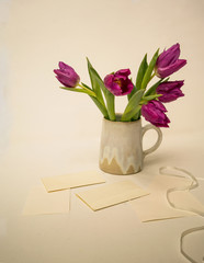 Pink tulips in a ceramic vase on a table with letters and envelopes