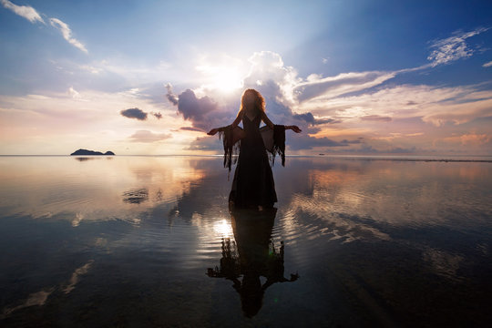 Elegant woman walking on water. Sunset and silhouette.