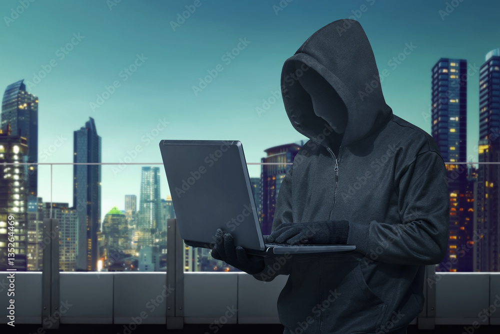 Poster hooded hacker with vendetta mask stealing information with laptop