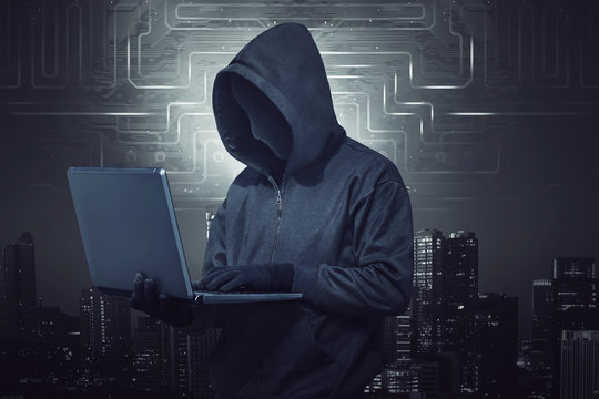 Hooded hacker holding laptop while typing