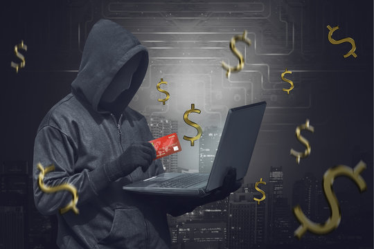 Hooded man wearing anonymous mask and holding laptop while showing credit card