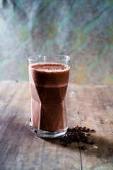 Spicy, frothy chili coffee smoothie and whole coffee beans on a textured wooden surface with...