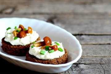 Canape with cottage cheese, mushrooms and green onion on a plate on a wooden background with copy space for text. Canape made from rye bread, soft cheese and canned mushrooms. Closeup