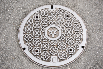In the picture we can see a circular design of a classic art on a manhole cover. The art looks very neat and clean. It is made of steel and concrete.