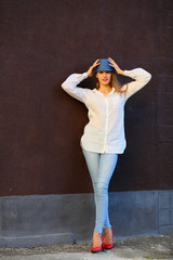 Fototapeta premium Young woman standing in red shoes near wall holding hat