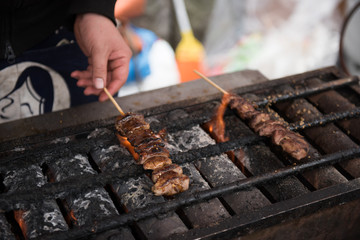In the picture we can see a man frying a food on a grill. The food is getting prepared on a wooden rack over a open fire.