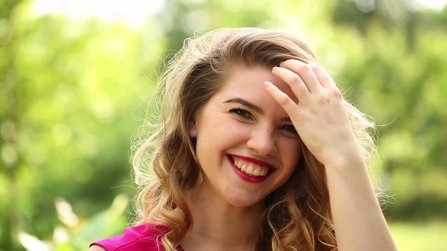 Young attractive girl in red dress corrects hair and laughs. Spring mood. She flirts. Curly hair and sexy lips.