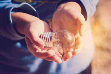 lamp bulb in children palm hands. energy saving concept for tomo