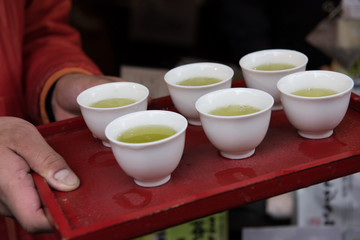 In the picture we can see a man holding a tray with six cups to serve hot green tea. Green tea is very popular in Japan.