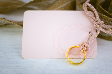 Blank pink paper card and gold ring on white wood background for
