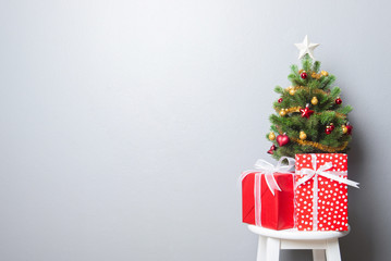 Gift boxes and small decorated Christmas tree on gray wall