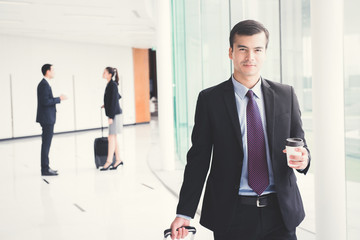 Businessman pulling baggage and holing coffee cup while walking in building hallway