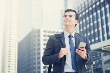 Fototapeta premium Young businessman using mobile phone while carrying bag in the city