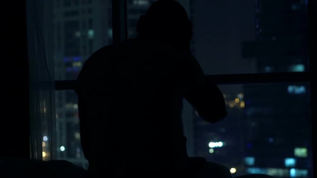 Silhouette of man having problems with sleep, waking up and standing by window at night
