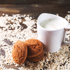 Oatmeal cookies on a background of oats, next to a glass of milk, on vintage board