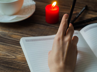 Close up of female hands writing with pencil at cafe with burning candle