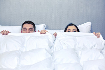 happy couple hiding under blanket in bed