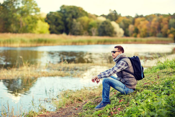 man with backpack resting on river bank