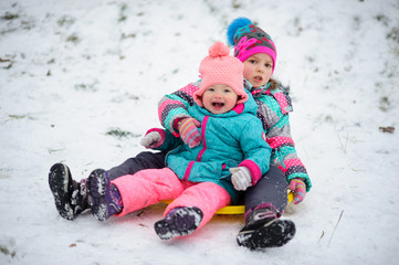 Two little girls together move down from a hill on the saucer sled.