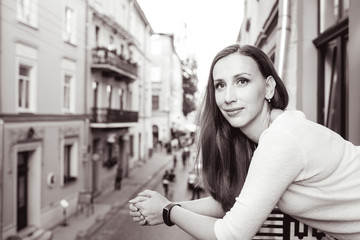 Young beautiful woman standing on the balcony and looking out on street of european city