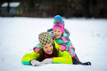 Lovely young woman and girl in bright jackets lie on snow.