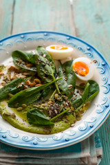 Spinach with avocado sauce and eggs on the light blue background vertical