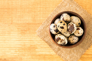 Quail eggs in a bowl on sacking on a wooden surface
