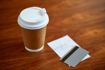 coffee in paper cup, bill and credit card on table