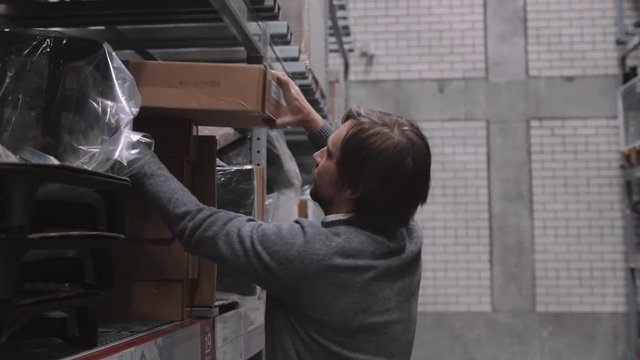 worker moving, taking out, putting, segregating, lifting on (from) shelves in warehouse. Man with box in modern stock