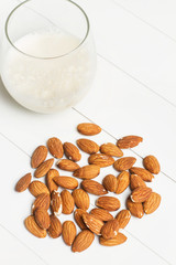 Vaso de leche de almendras sobre mesa de madera blanca. Vista superior