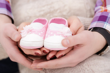 Obraz na płótnie Canvas pink booties for newborn baby in hands of mum and dad. pregnancy