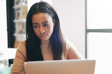 Digital marketing specialist is working on a new promotion project by a portable computer while sitting in a modern coffee shop during lunch time. Freelancer female is communicating with customers.