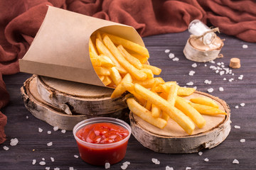 The scattered French fries with ketchup on wooden saw cuts with salt