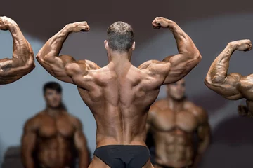 Foto op Plexiglas Bodybuilder flexing back and biceps. Muscular athlete posing on stage. Top sportsmen at bodybuilding competition. Opponents are watching. © DenisProduction.com
