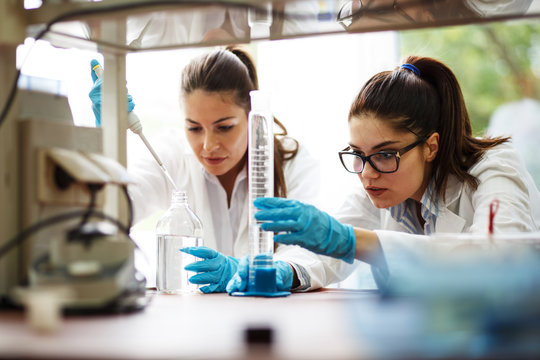 Two dedicated female lab scientists meticulously work together, focusing on chemical research and experiments, advancing scientific knowledge.