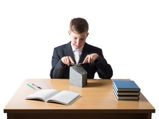Young boy in a jacket sitting at work desk with notebook and books and holding a fork with a knife and gladly cut a piece of granite on a white background