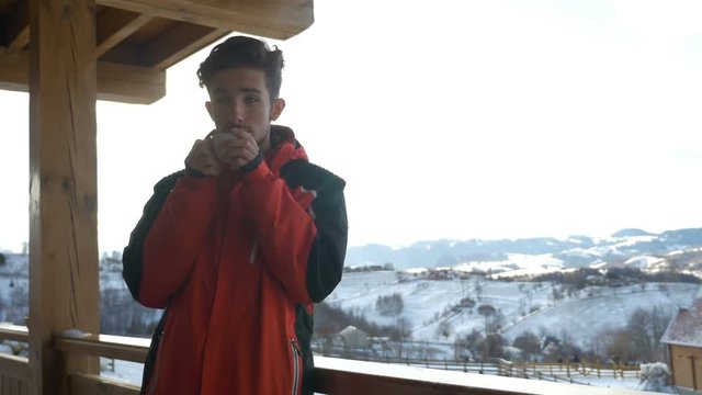 Guy grabbing a cup of hot beverage from a wooden railing on a deck in winter and drinking it