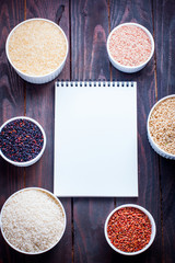 Several types of rice on the table with culinary notebook, top view