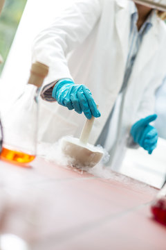 Young female scientist in lab coat wearing gloves, doing experiments in lab.