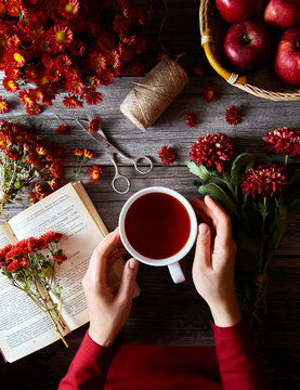 Cup of hot tea or rooibos in female hands on a wooden table with flowers, book and apple. The concept of warm days of summer or spring.