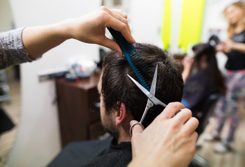 Unrecognizable hairdresser cutting hair of her young client.