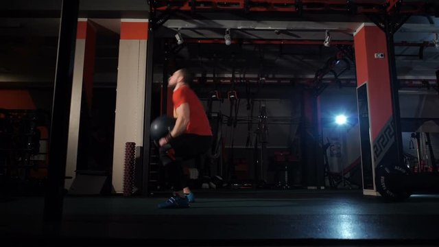 A young man picks up a heavy ball sports