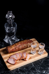 Bottle and shot glasses with vodka with slices of smoked meat on