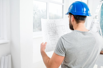 Handsome repairman or builder in helmet working with drawings on renovation of interior