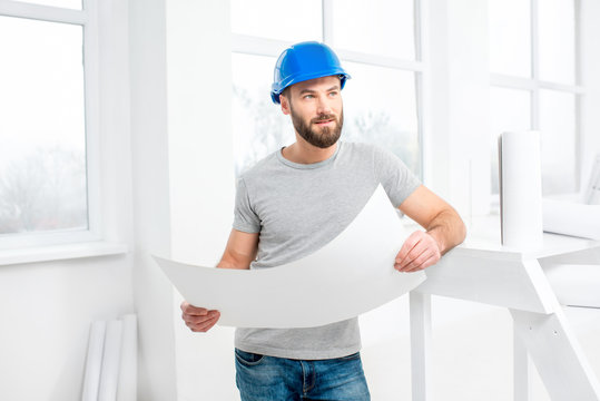 Handsome repairman or builder in helmet working with drawings on renovation of apartment interior