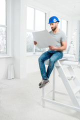 Handsome repairman or builder in helmet working with drawings on renovation of apartment interior