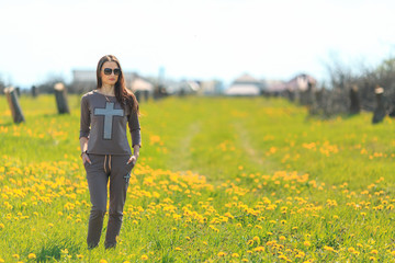 Young beautiful white girl in a brown sports suit stands in a field of yellow dandelions. Spring portrait.