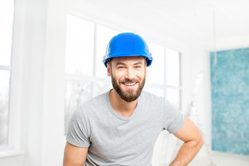 Portrait of a handsome builder, foreman or repairman in the helmet in the white interior