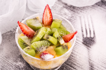 A kiwi, strawberry and orange in a vase against a dark background with icing sugar 