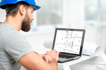 Handsome architect or foreman in helmet working with laptop on the apartment drawings at the...